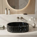 Black marble finish oval table top wash basin with white veining, sculpted vertical fluted exterior and 20 inch countertop design for modern luxury bathrooms.
