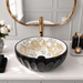 Glossy black round tabletop wash basin with a scalloped exterior and beige floral design on a white interior.