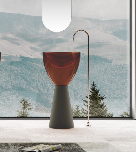 A free-standing, transparent resin wash basin with a pedestal base, placed in a room with a scenic view.