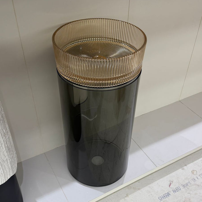 Black cylindrical trash bin with a gold top on a tiled floor.