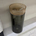 Black cylindrical trash bin with a gold top on a tiled floor.
