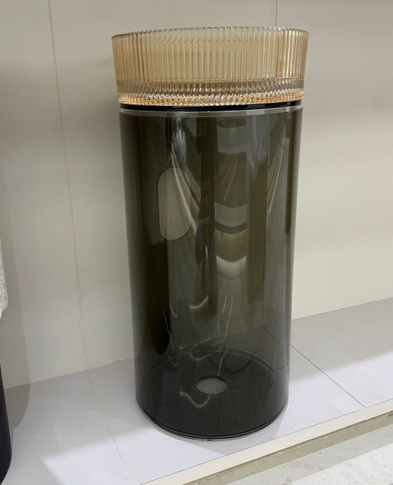 Black cylindrical container with a ribbed gold lid on a white surface.